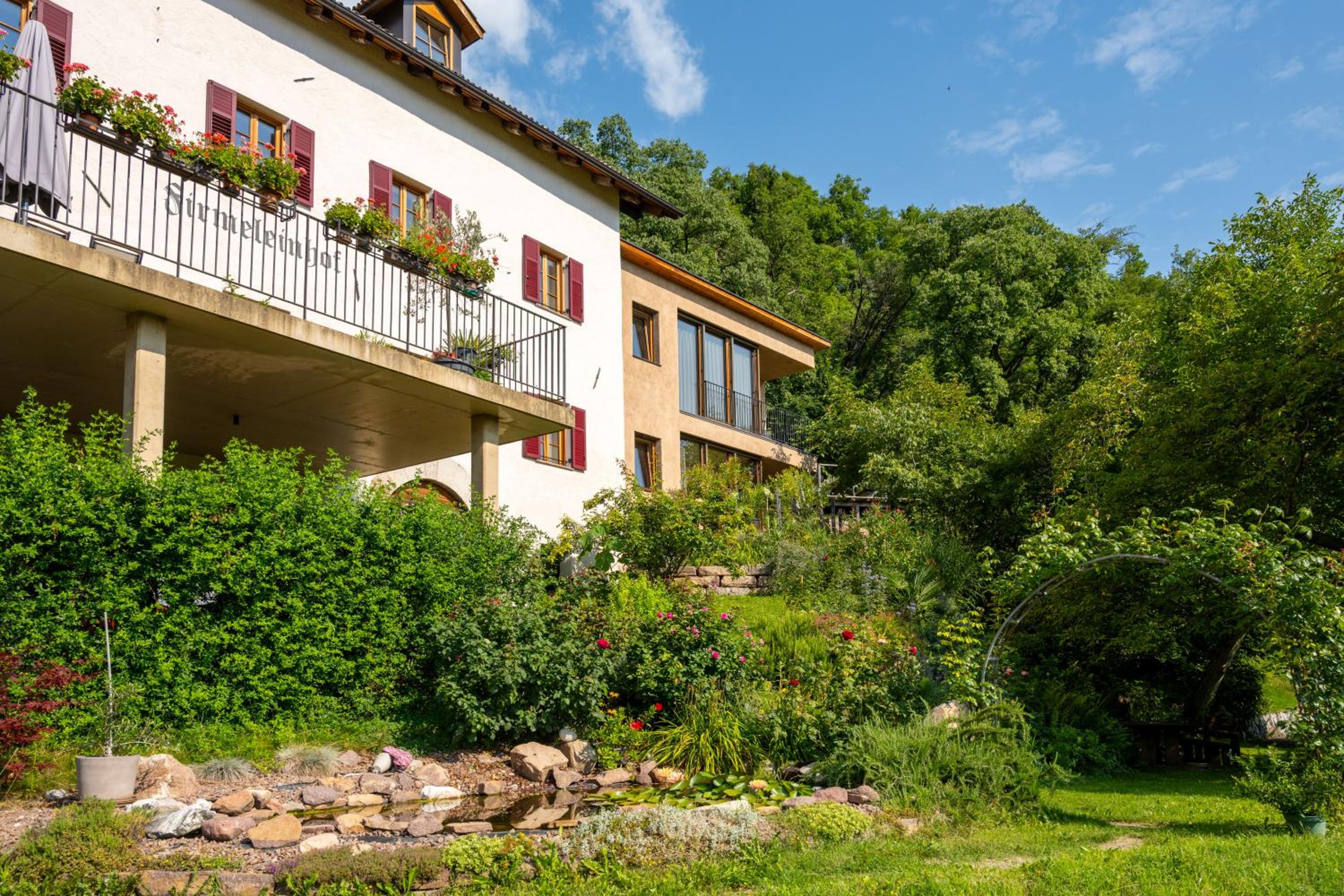Firmeleinhof mit Balkon, moderner Glasfront und grünem Garten mit Teich
