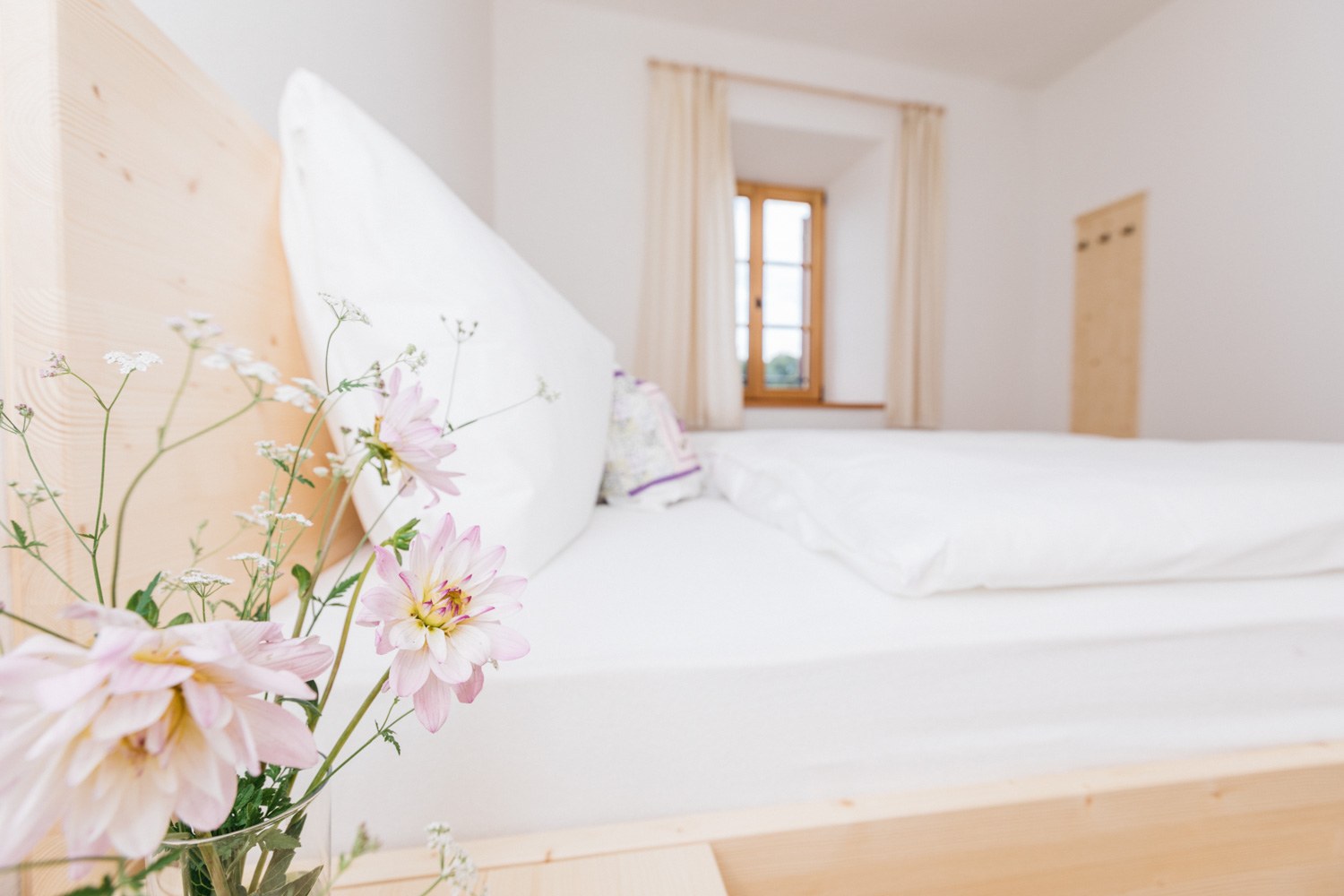 Helles Schlafzimmer mit Holzbett und frischen Blumen